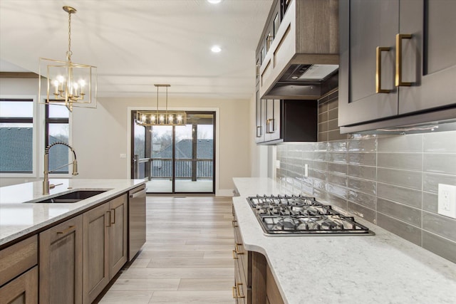 kitchen with backsplash, a sink, light stone counters, appliances with stainless steel finishes, and wall chimney exhaust hood