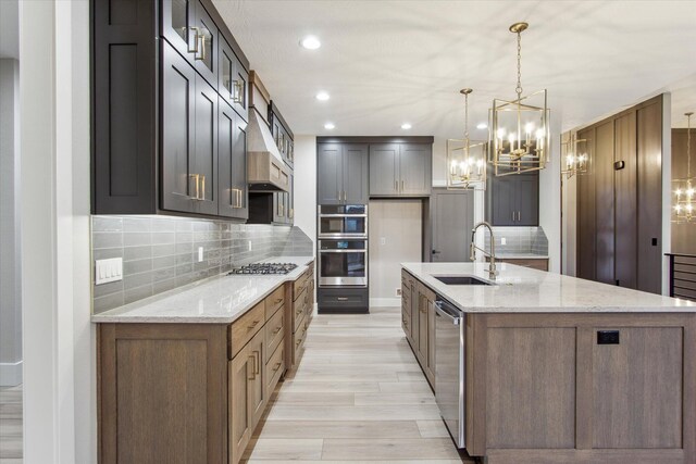 kitchen with a sink, stainless steel appliances, custom exhaust hood, and a notable chandelier