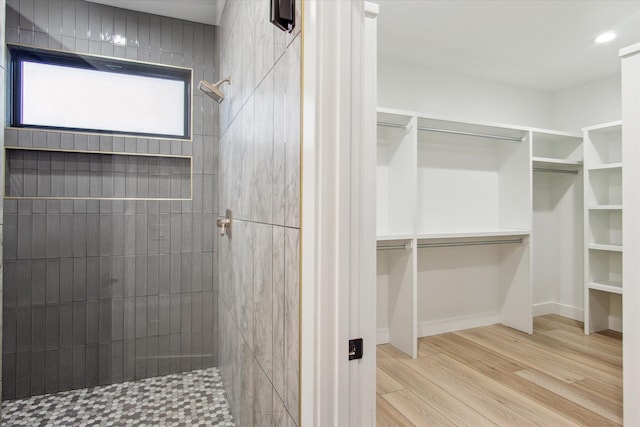 bathroom with baseboards, wood finished floors, recessed lighting, tiled shower, and a walk in closet