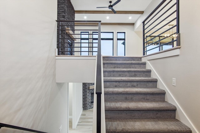 stairs featuring ceiling fan, wood finished floors, and beamed ceiling