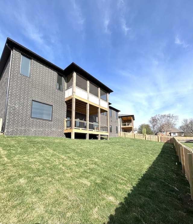 back of house with a lawn, fence, and brick siding
