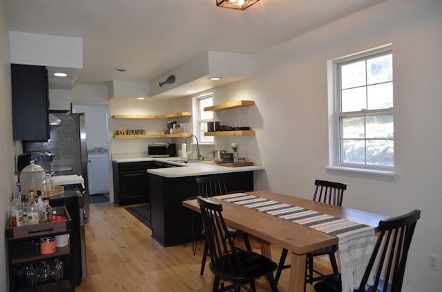 kitchen with tasteful backsplash, black refrigerator, sink, kitchen peninsula, and light hardwood / wood-style flooring