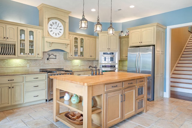 kitchen featuring stainless steel appliances, pendant lighting, light stone countertops, decorative backsplash, and a kitchen island with sink