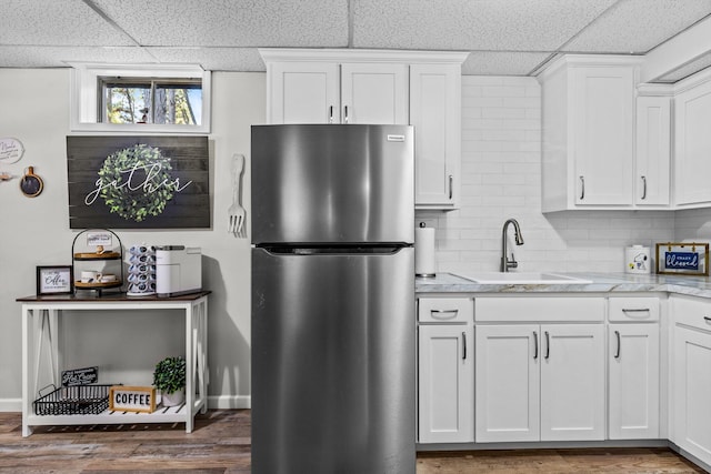 kitchen featuring white cabinetry, sink, stainless steel fridge, light stone counters, and a drop ceiling