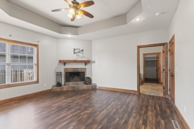 unfurnished living room with a fireplace, dark hardwood / wood-style flooring, a tray ceiling, and ceiling fan