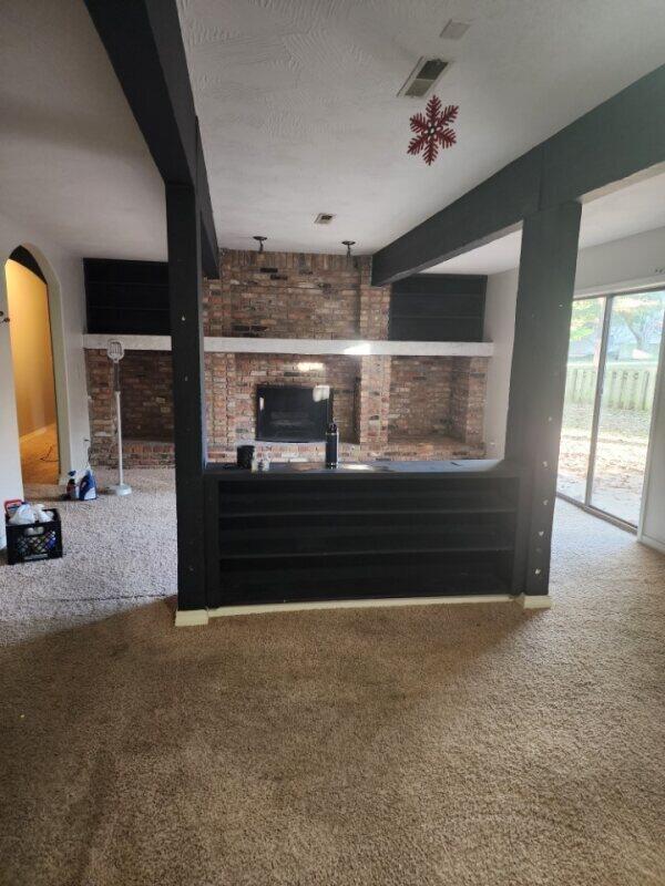 unfurnished living room with a textured ceiling, carpet, brick wall, and beamed ceiling