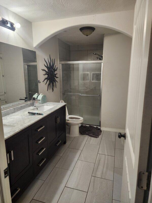 bathroom with toilet, vanity, a textured ceiling, and a shower with door