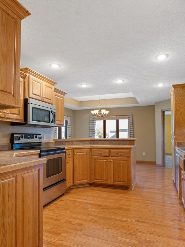 kitchen featuring light hardwood / wood-style floors, a notable chandelier, a textured ceiling, a tray ceiling, and appliances with stainless steel finishes