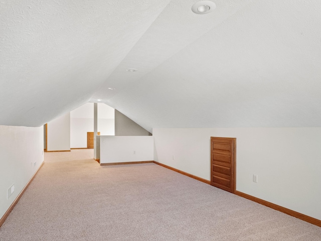 additional living space featuring a textured ceiling, light carpet, and vaulted ceiling