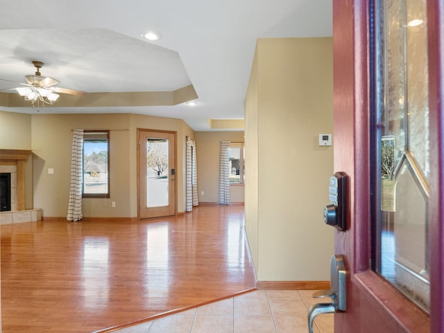 entrance foyer with ceiling fan, a tiled fireplace, a raised ceiling, and light hardwood / wood-style flooring