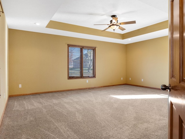 empty room featuring a tray ceiling, light colored carpet, and ceiling fan