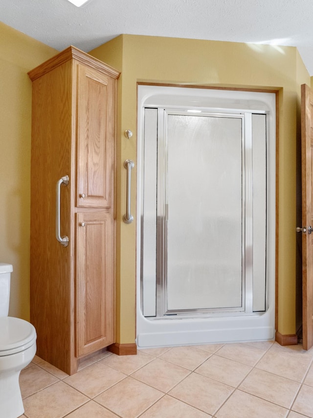 bathroom featuring toilet, a textured ceiling, tile patterned floors, and a shower with door