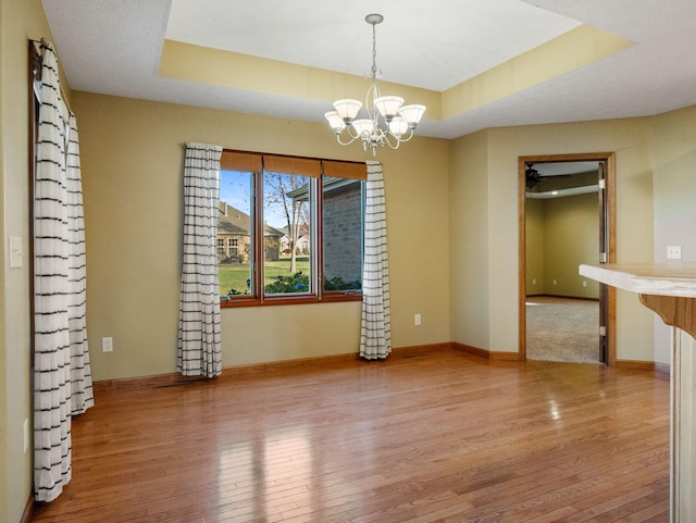 empty room with hardwood / wood-style floors, a raised ceiling, and an inviting chandelier