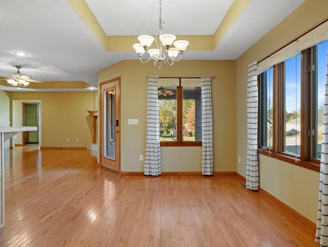 unfurnished room with ceiling fan with notable chandelier, light hardwood / wood-style flooring, and a raised ceiling