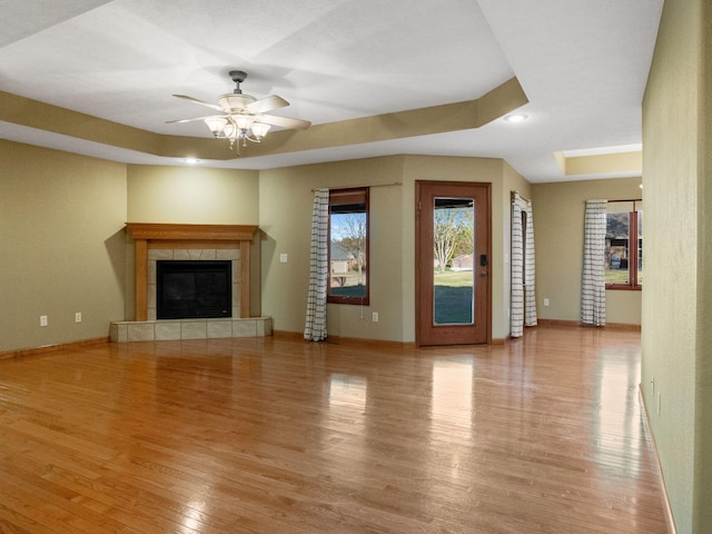 unfurnished living room with ceiling fan, a raised ceiling, light hardwood / wood-style floors, and a fireplace