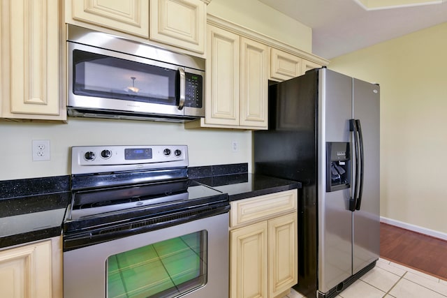 kitchen with appliances with stainless steel finishes, cream cabinets, dark stone counters, and light hardwood / wood-style flooring