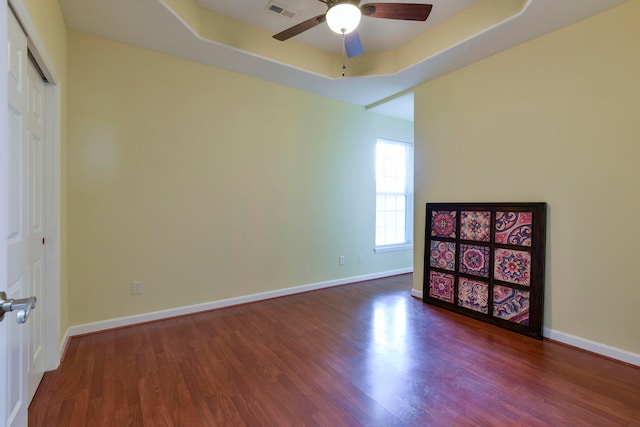 spare room with dark wood-type flooring, ceiling fan, and a tray ceiling