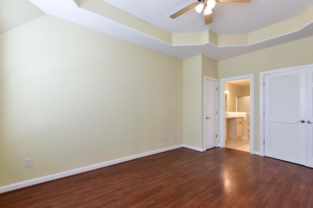 unfurnished bedroom with dark wood-type flooring, ceiling fan, connected bathroom, and a tray ceiling