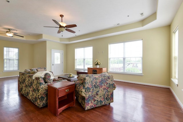 living room with dark hardwood / wood-style flooring, ceiling fan, and a tray ceiling