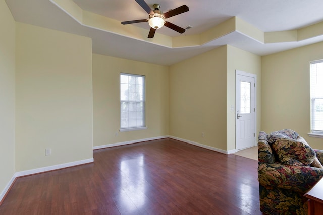 unfurnished living room with dark wood-type flooring, ceiling fan, plenty of natural light, and a raised ceiling