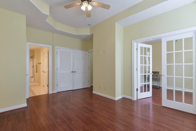 unfurnished bedroom featuring ensuite bathroom, ceiling fan, dark wood-type flooring, a closet, and french doors