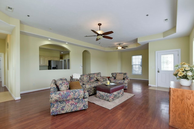 living room featuring dark hardwood / wood-style flooring, ceiling fan, and a raised ceiling