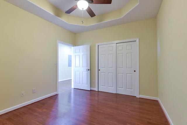 unfurnished bedroom featuring dark wood-type flooring, a closet, a tray ceiling, and ceiling fan