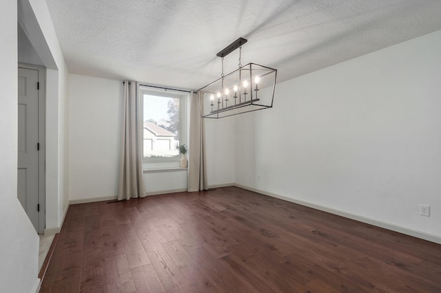 unfurnished dining area featuring dark wood-type flooring, a textured ceiling, and a notable chandelier