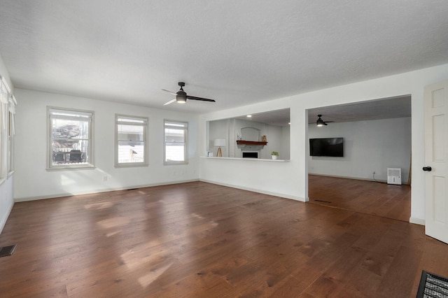 unfurnished living room featuring ceiling fan, a healthy amount of sunlight, a textured ceiling, and dark hardwood / wood-style flooring