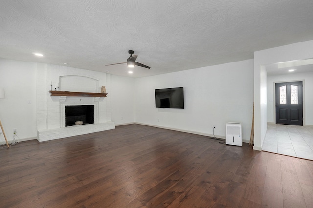 unfurnished living room featuring dark wood-type flooring, a textured ceiling, ceiling fan, and a brick fireplace