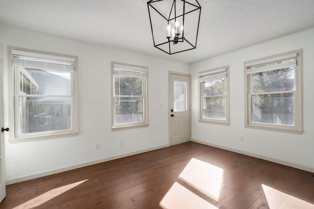 unfurnished dining area featuring plenty of natural light, dark wood-type flooring, and a notable chandelier