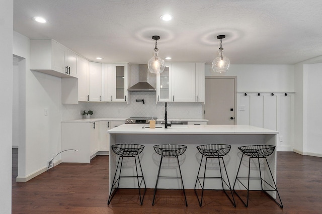 kitchen featuring white cabinets, a kitchen island with sink, and wall chimney range hood