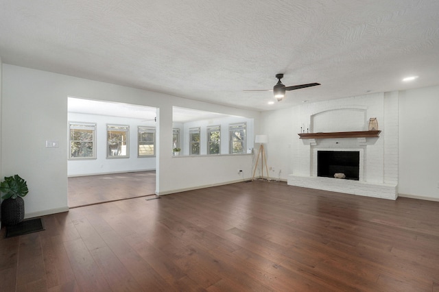 unfurnished living room featuring ceiling fan, a textured ceiling, dark hardwood / wood-style floors, and a brick fireplace