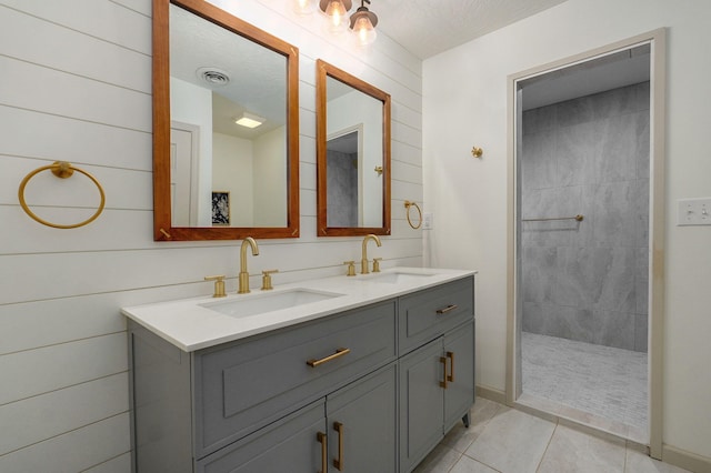 bathroom featuring wood walls, a textured ceiling, vanity, tiled shower, and tile patterned floors