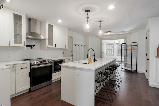 kitchen with a center island with sink, wall chimney exhaust hood, white cabinetry, and stainless steel range with electric stovetop