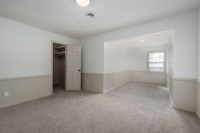 unfurnished bedroom featuring carpet flooring, a spacious closet, a textured ceiling, and a closet