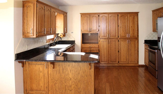 kitchen with sink, tasteful backsplash, dark hardwood / wood-style flooring, kitchen peninsula, and dark stone countertops