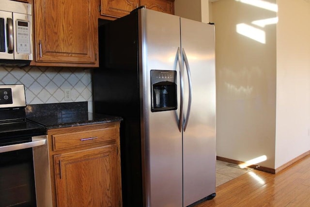 kitchen with appliances with stainless steel finishes, backsplash, light hardwood / wood-style floors, and dark stone counters