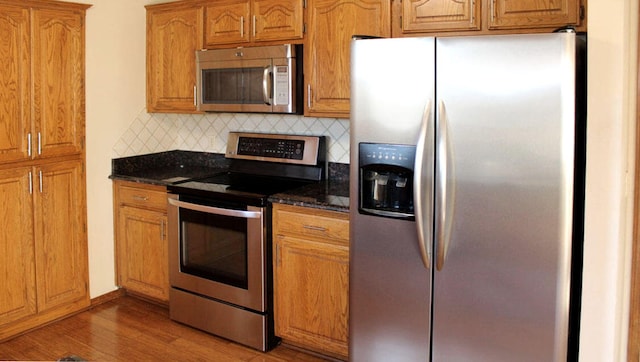 kitchen featuring dark stone counters, decorative backsplash, stainless steel appliances, and dark hardwood / wood-style floors