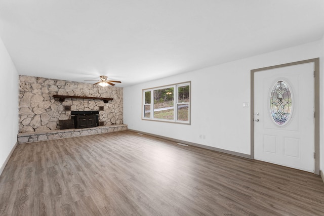 unfurnished living room with a wood stove, wood-type flooring, and ceiling fan