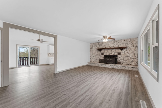 unfurnished living room with a wood stove, wood-type flooring, and ceiling fan