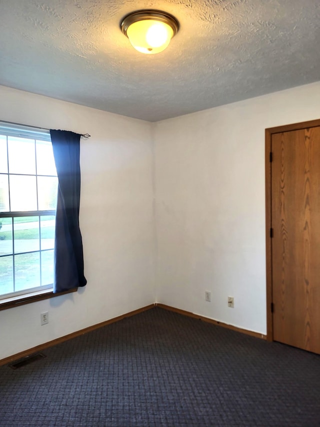 empty room featuring a textured ceiling and dark carpet