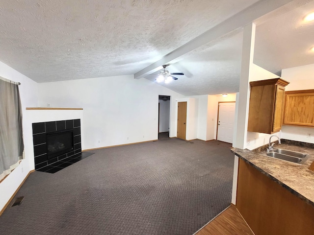 unfurnished living room with dark colored carpet, sink, a textured ceiling, vaulted ceiling with beams, and a tile fireplace