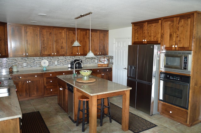 kitchen with stainless steel appliances, decorative backsplash, a kitchen island with sink, a kitchen breakfast bar, and decorative light fixtures