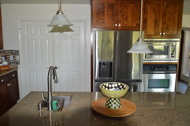 kitchen featuring appliances with stainless steel finishes, pendant lighting, decorative backsplash, sink, and dark stone countertops