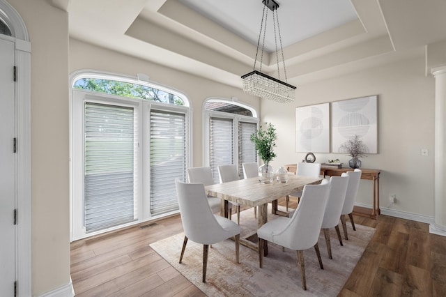 dining space with light wood-type flooring, a raised ceiling, and decorative columns