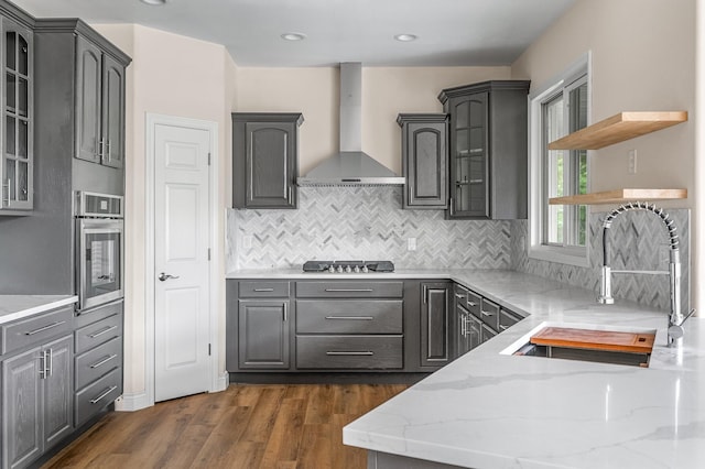 kitchen featuring sink, light stone countertops, stainless steel oven, wall chimney range hood, and dark hardwood / wood-style flooring