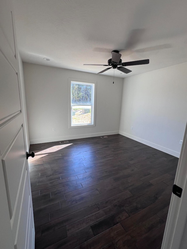 spare room with dark wood-type flooring, ceiling fan, and baseboards