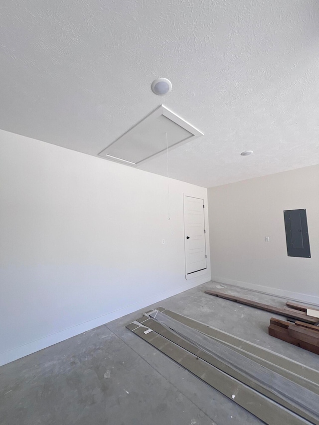 interior space with attic access, electric panel, baseboards, and a textured ceiling