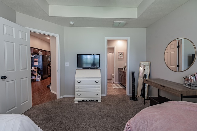 carpeted bedroom featuring ensuite bathroom, a textured ceiling, and black refrigerator